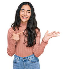 Hispanic teenager girl with dental braces wearing casual clothes amazed and smiling to the camera...