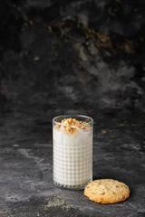Sierkussen Vertical closeup of a white smoothie in a clear glass with a cookie beside it on a dark background. © Galip Kürkcü/Wirestock Creators