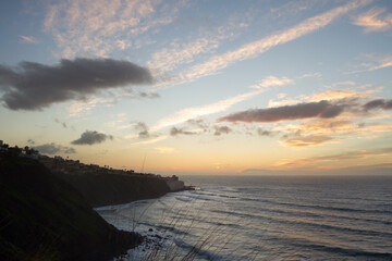 beautiful seascape at sunset. Silhouette of a fishing village. The sun sets on the horizon behind the sea. Pink and golden clouds in blue sky. Bajamar, Tenerife, Canary Islands.  