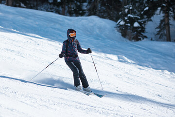 Fototapeta na wymiar Amateur female skier sliding down the slope on a sunny day at a mountain resort.