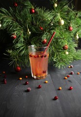 Winter drink glass with buckthorn and cranberries and straw, christmas pine tree decoration on black wooden table