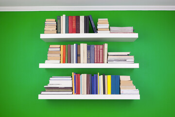 neat stacks and rows of books on white shelves against a green wall