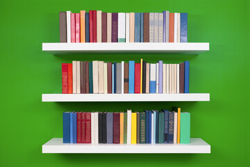 neat rows of books on white shelves against a green wall