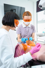Young woman in protective glasses lies in a dental chair