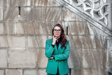a girl in a green suit and glasses stands near the wall