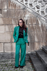 Fototapeta na wymiar a girl in a green suit and glasses stands near the wall