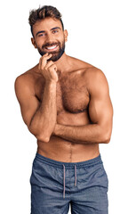 Young hispanic man wearing swimwear shirtless looking confident at the camera with smile with crossed arms and hand raised on chin. thinking positive.
