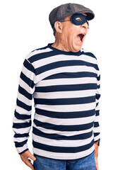 Senior handsome man wearing burglar mask and t-shirt angry and mad screaming frustrated and furious, shouting with anger. rage and aggressive concept.