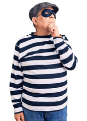 Senior handsome man wearing burglar mask and t-shirt with hand on chin thinking about question,...