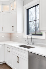 Fototapeta na wymiar A luxurious modern white kitchen with white cabinets, beautiful granite, and hardwood floors. The kitchen sink has a chrome faucet and a deep, stainless steel tub.