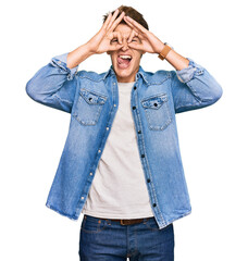 Handsome caucasian man wearing casual denim jacket doing ok gesture like binoculars sticking tongue out, eyes looking through fingers. crazy expression.
