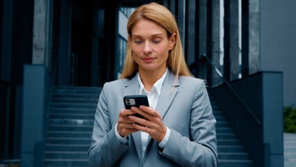 Young woman stand on downtown with phone in hands typing business email answering message in social media smiling businesswoman using mobile application for remote internet communication on smartphone