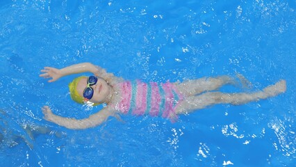 A little girl swims on her back in the pool. Child, girl learns to swim in the pool. A cute little...