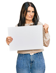 Fototapeta premium Middle age brunette woman holding blank empty banner screaming proud, celebrating victory and success very excited with raised arms