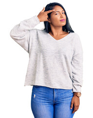 Hispanic woman with long hair wearing casual clothes pointing unhappy to pimple on forehead, ugly...