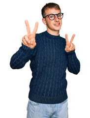 Young blond man wearing casual clothes and glasses smiling looking to the camera showing fingers...