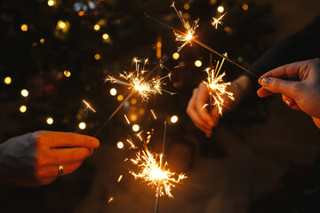 Hands holding fireworks against christmas lights in dark room. Happy New Year! Atmospheric holiday....