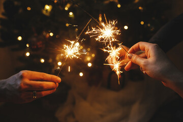 Hands holding fireworks against christmas lights in dark room. Happy New Year! Atmospheric holiday....