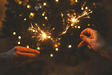 Happy New Year! Couple celebrating with burning sparklers in hands on background of stylish...