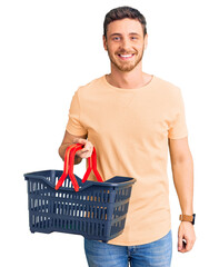 Handsome young man with bear holding supermarket shopping basket looking positive and happy...