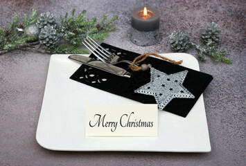 Festive Christmas table with plates and cutlery in black and white colors. Christmas greeting on a place card Merry Christmas.