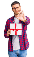 Handsome young man with bear holding gift with open hand doing stop sign with serious and confident expression, defense gesture