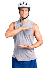 Young handsome man wearing bike helmet gesturing with hands showing big and large size sign, measure symbol. smiling looking at the camera. measuring concept.