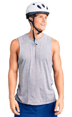 Young handsome man wearing bike helmet looking away to side with smile on face, natural expression. laughing confident.