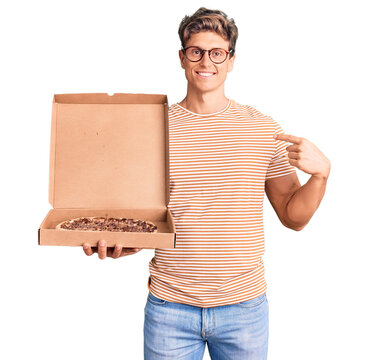 Young handsome man holding delivery pizza box pointing finger to one self smiling happy and proud