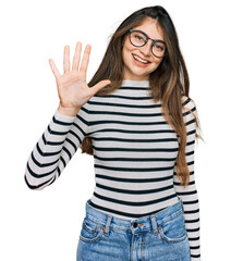 Obraz na płótnie Canvas Young beautiful teen girl wearing casual clothes and glasses showing and pointing up with fingers number five while smiling confident and happy.