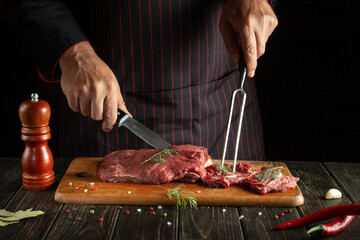 The chef prepares veal with his hands in the kitchen. Menu idea for a restaurant or hotel on a dark background