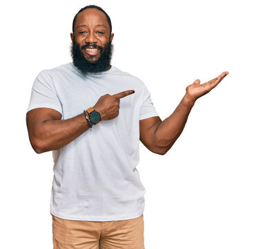 Young african american man wearing casual white tshirt amazed and smiling to the camera while presenting with hand and pointing with finger.