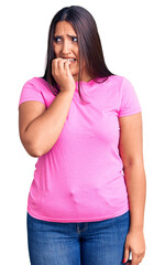 Young beautiful brunette woman wearing casual t-shirt looking stressed and nervous with hands on mouth biting nails. anxiety problem.