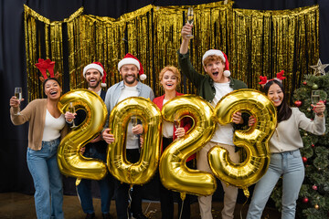 Cheerful interracial business people holding champagne and balloons in shape of 2023 in office
