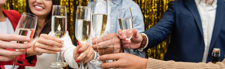 Cropped view of multiethnic business people holding glasses of champagne near tinsel in office, banner