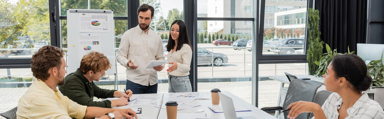 interracial colleagues with digital tablet talking to business team in meeting room, banner