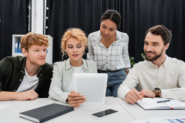 blonde businesswoman holding digital tablet while working with interracial team in office