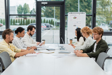 multiethnic business people working with gadgets and documents at conference table in office