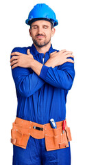 Young handsome man wearing worker uniform and hardhat hugging oneself happy and positive, smiling confident. self love and self care