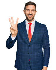 Handsome man with beard wearing business suit and tie showing and pointing up with fingers number three while smiling confident and happy.