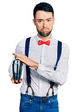 Hispanic man with beard preparing cocktail mixing drink with shaker depressed and worry for distress, crying angry and afraid. sad expression.