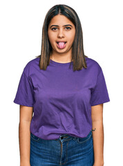 Fototapeta premium Young hispanic girl wearing casual purple t shirt sticking tongue out happy with funny expression. emotion concept.