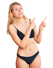Young beautiful blonde woman wearing bikini pointing aside worried and nervous with both hands, concerned and surprised expression