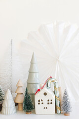 Stylish little Christmas trees, houses and candy cane on white table. Merry Christmas and Happy Holidays! Modern festive scene, miniature snowy village. Winter banner, scandinavian decor