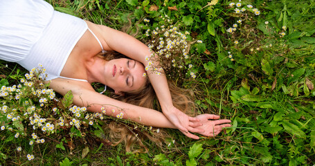 Portrait of sexy cute young blonde woman in white dress lying in the grass with daisies