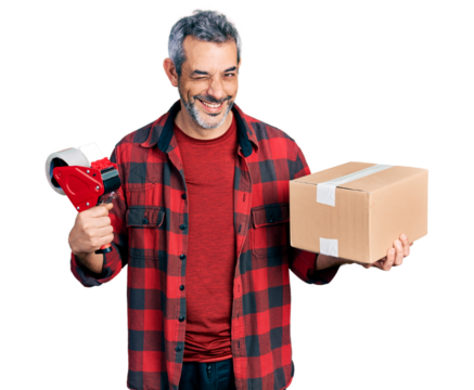 Middle age hispanic with grey hair holding packing tape and cardboard box winking looking at the camera with sexy expression, cheerful and happy face.