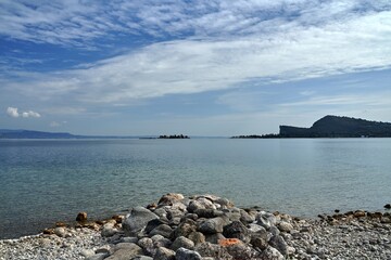 Fototapeta na wymiar Boulders on the beach, island and mountains at Lake Garda