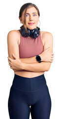 Beautiful caucasian young woman wearing gym clothes and using headphones shaking and freezing for...