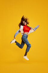 Fototapeta na wymiar Portrait of young beautiful girl posing in stylish casual clothes, cheerfully jumping isolated over yellow background