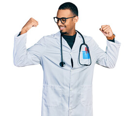 Young african american man wearing doctor uniform and stethoscope showing arms muscles smiling proud. fitness concept.